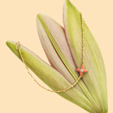 Tiny Jewels gold necklace with a red flower pendant on green leaves against a beige background