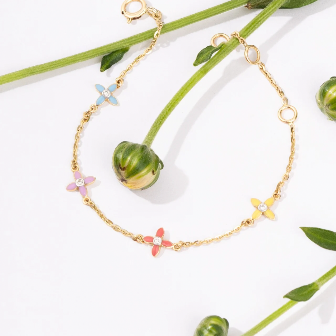 Tiny Jewels gold bracelet with colorful flower-shaped charms on a white background with green leaves.