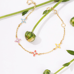 Tiny Jewels gold bracelet with colorful flower-shaped charms on a white background with green leaves.