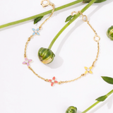 Tiny Jewels gold bracelet with colorful flower-shaped charms on a white background with green leaves.
