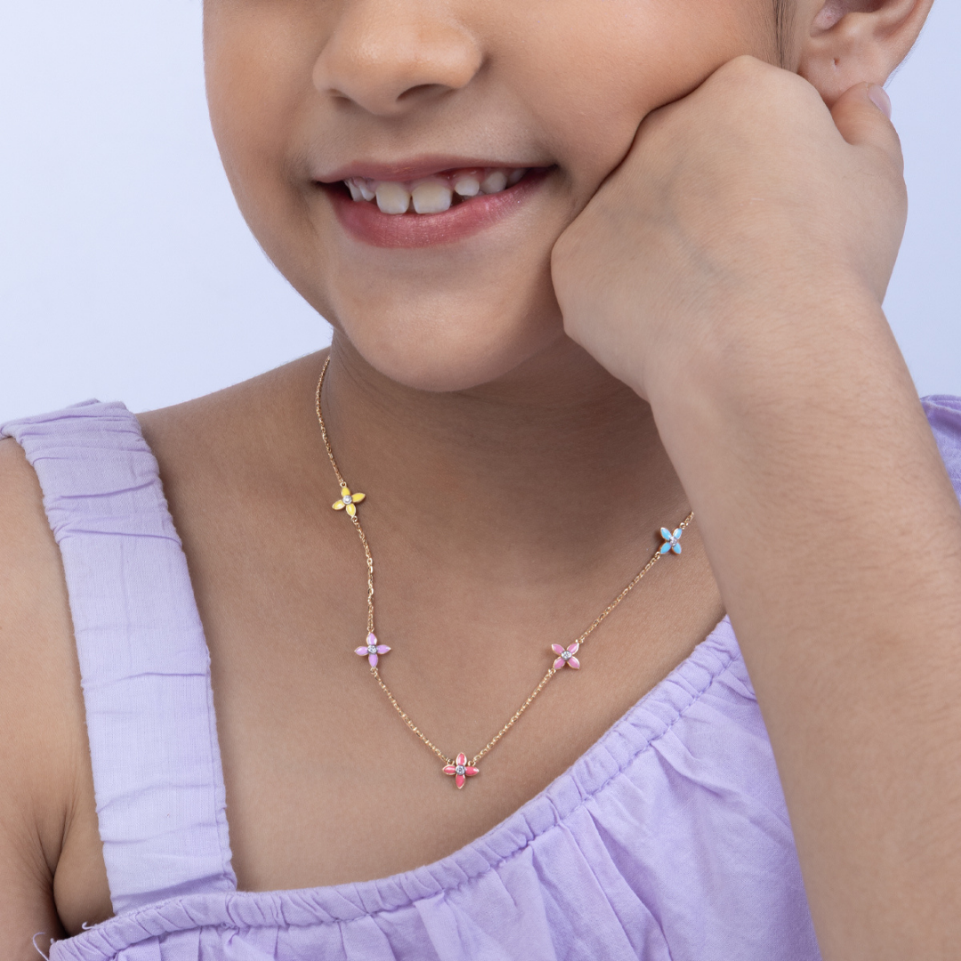 Tiny Jewels child wearing a delicate necklace with floral pendants against a light purple background