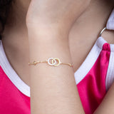 Tiny Jewels gold bracelet on a person's wrist with a pink and white top