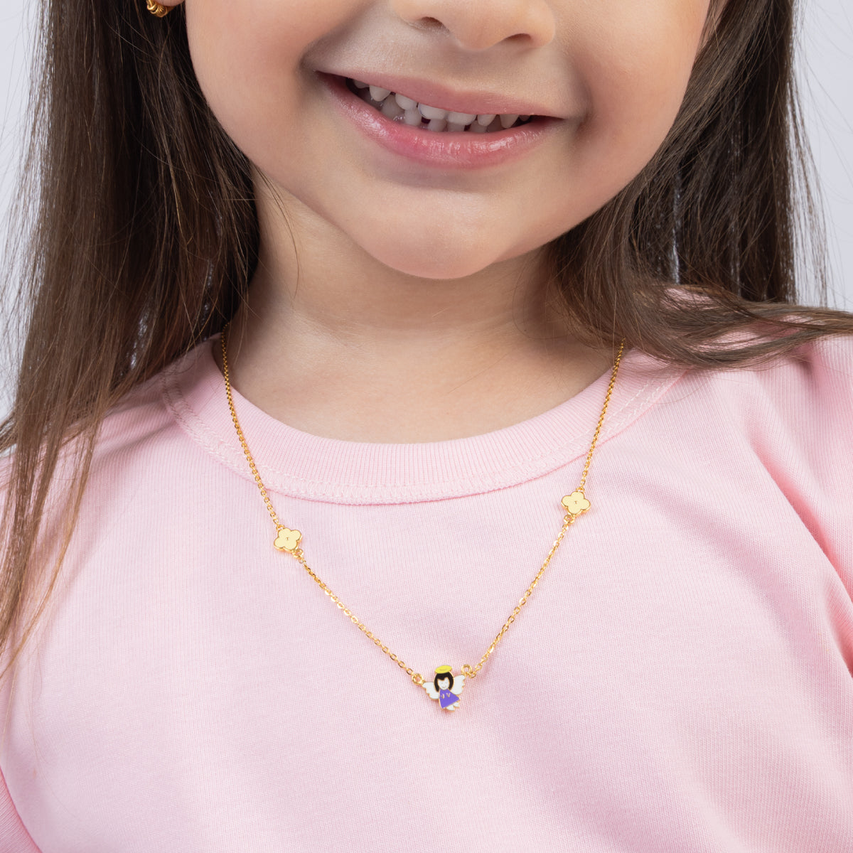 Tiny Jewels child wearing a gold necklace with a small pendant on a plain background