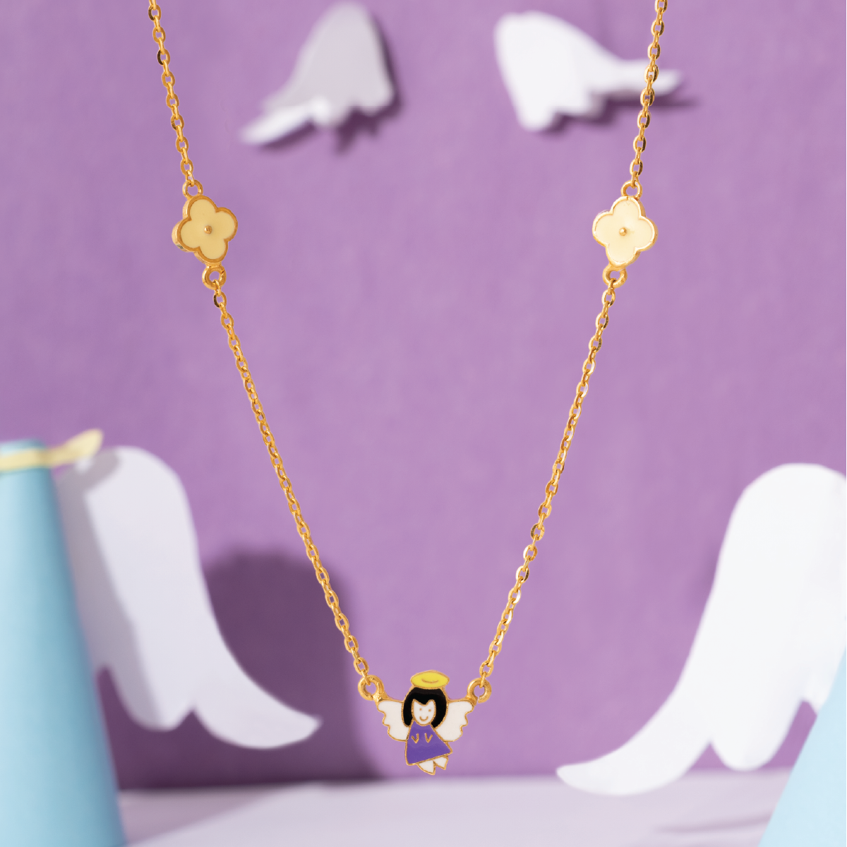 Tiny Jewels gold necklace with an angel pendant on a purple background