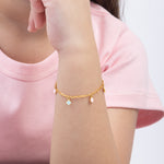 Tiny Jewels gold bracelet with small charms on a wrist against a pink shirt background