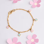 Tiny Jewels gold bracelet with flower charms on a light pink background with flowers