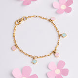 Tiny Jewels gold bracelet with flower charms on a light pink background with flowers