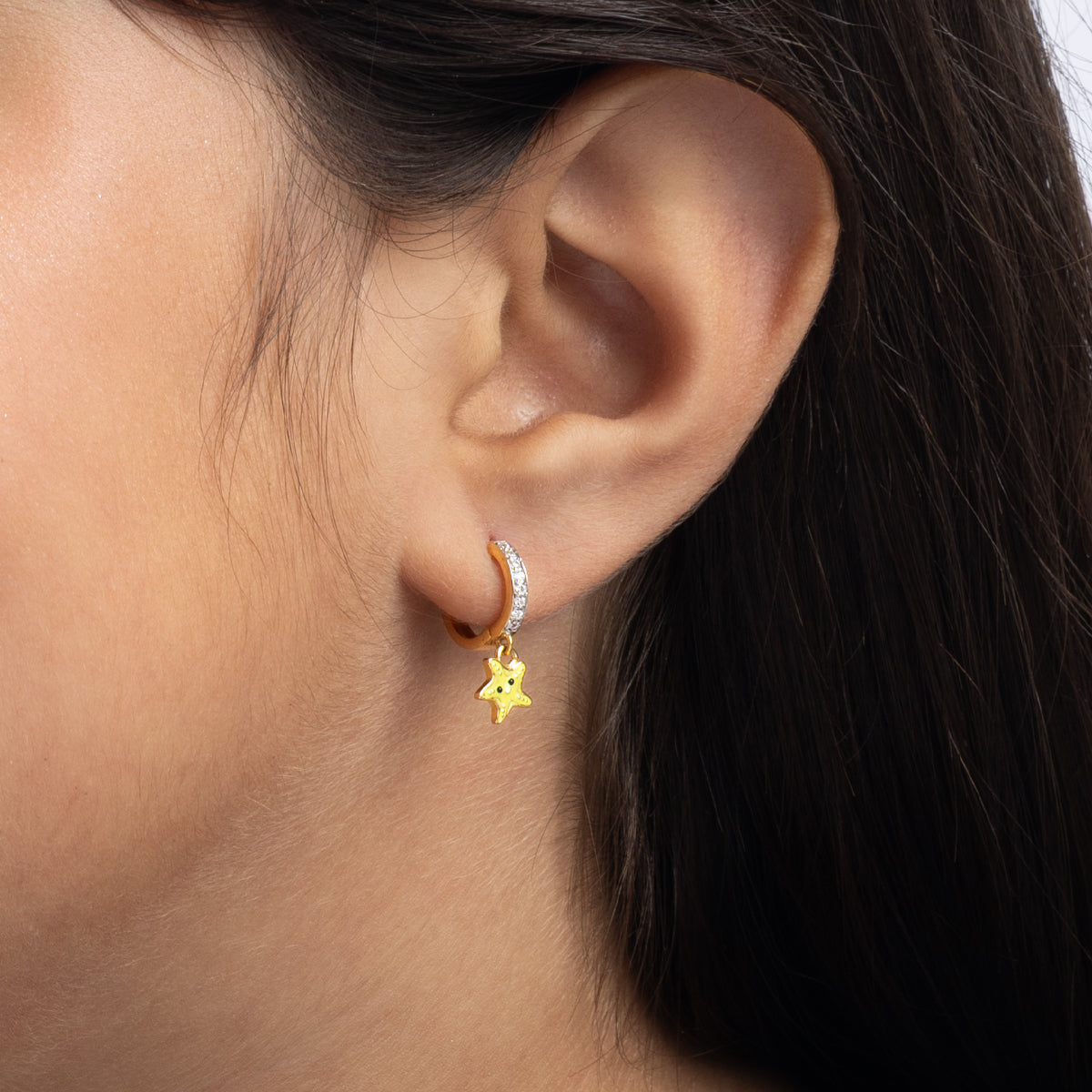 Tiny Jewels close-up of an ear wearing a gold hoop earring with a star charm.
