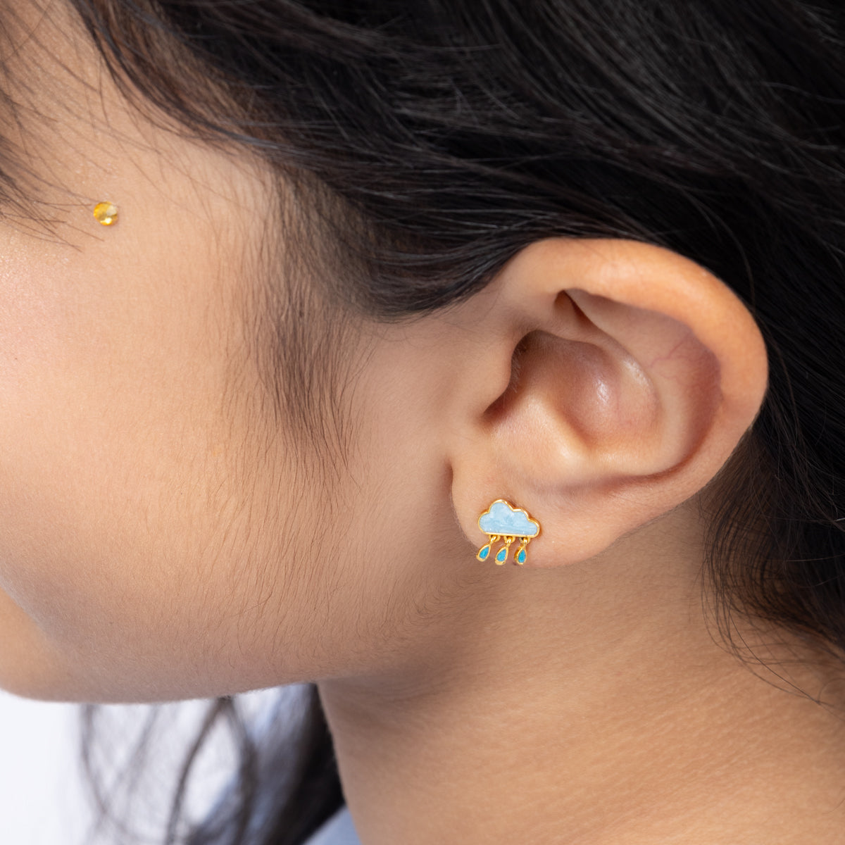 Tiny Jewels close-up of an ear wearing a cloud-shaped earring with raindrops.