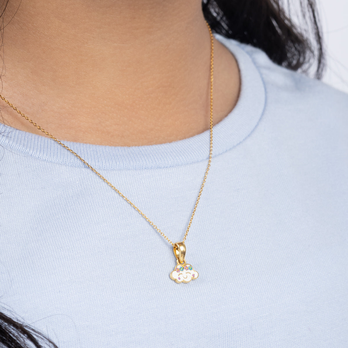 Tiny Jewels gold necklace with a small pendant worn by a person in a light blue shirt.
