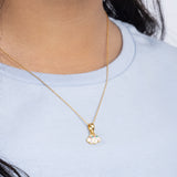 Tiny Jewels gold necklace with a small pendant worn by a person in a light blue shirt.