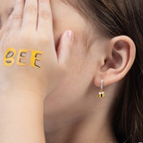 Tiny Jewels close-up of a person wearing a gold bee-shaped earring with a blurred background.