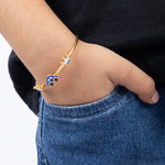 Tiny Jewels gold bracelet with blue and black accents on a wrist against a black shirt and blue jeans background