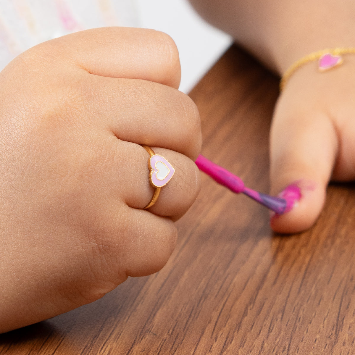 Tiny Jewels child's hand holding a pink nail polish brush on a wooden surface
