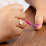 Tiny Jewels child's hand holding a pink nail polish brush on a wooden surface