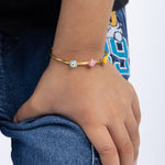 Tiny Jewels hand wearing a gold bracelet with colorful beads on a white background