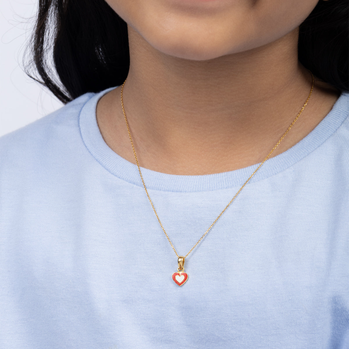Tiny Jewels person wearing a gold necklace with a heart-shaped pendant on a plain background
