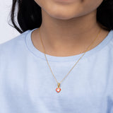 Tiny Jewels person wearing a gold necklace with a heart-shaped pendant on a plain background