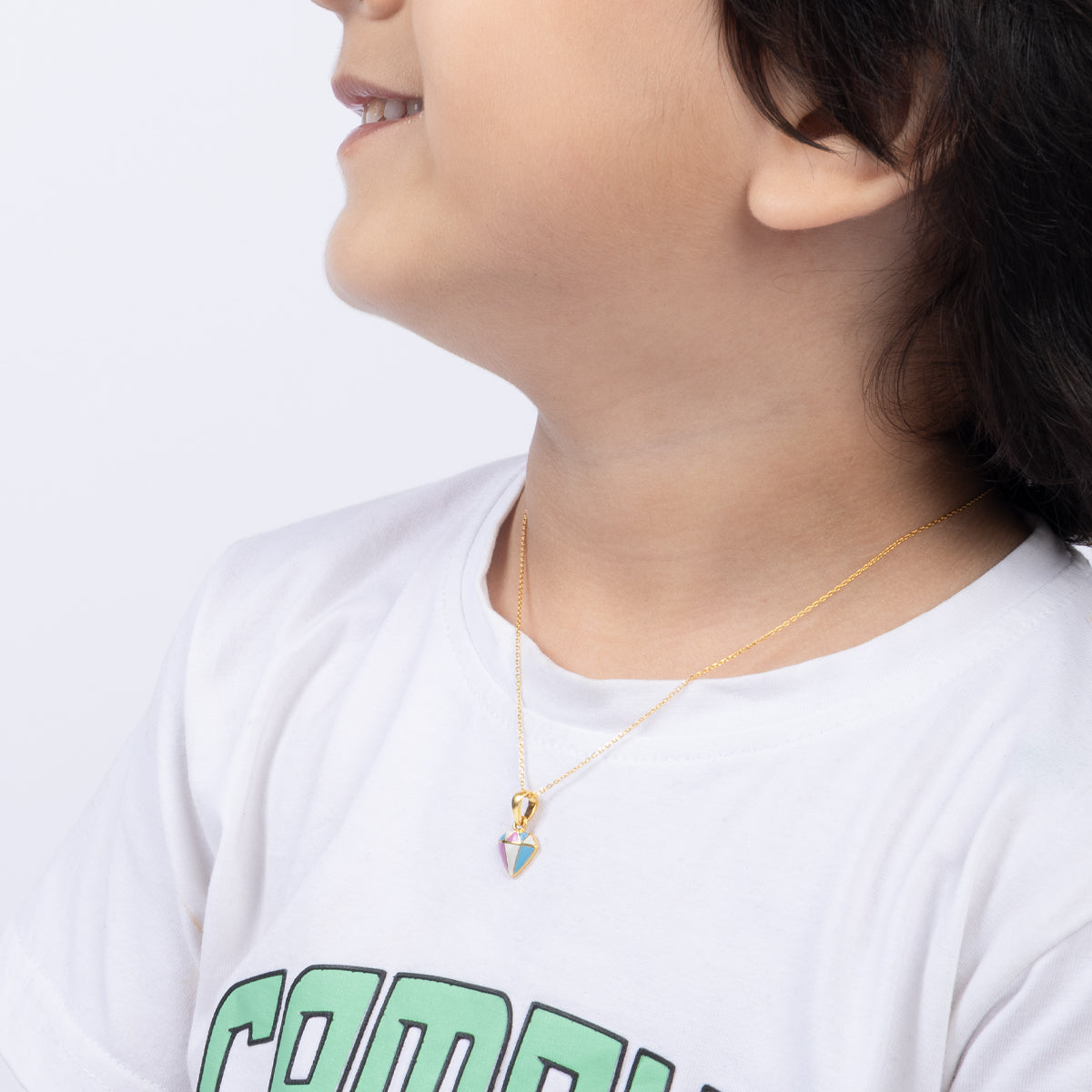 Tiny Jewels person wearing a white shirt with green text and a gold necklace with a pendant.