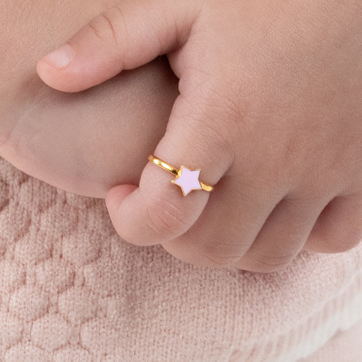 Tiny Jewels gold ring with a star design on a child's finger against a soft pink background