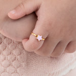 Tiny Jewels gold ring with a star design on a child's finger against a soft pink background