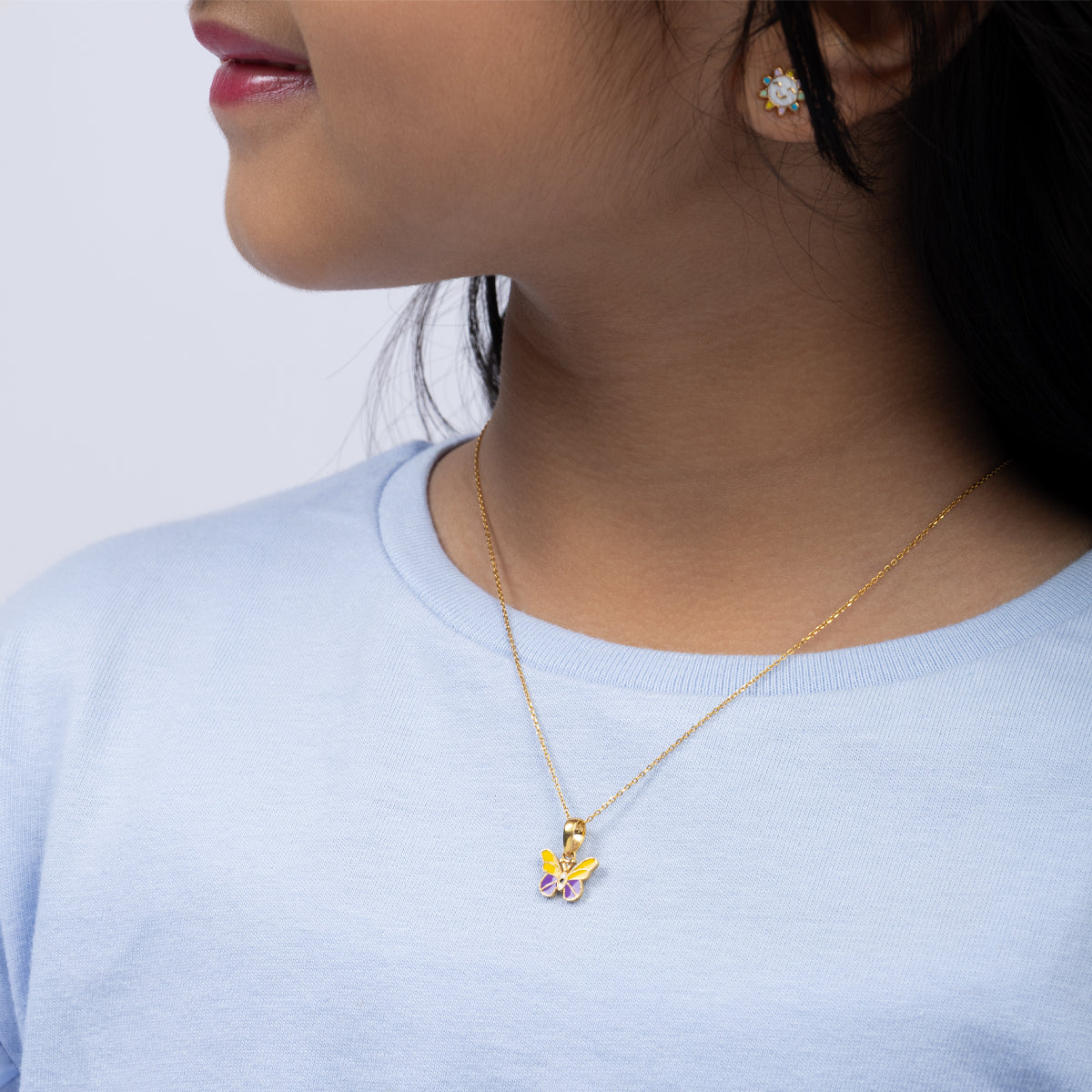 Tiny Jewels Close-up of a person wearing a gold necklace with a colorful pendant against a light background