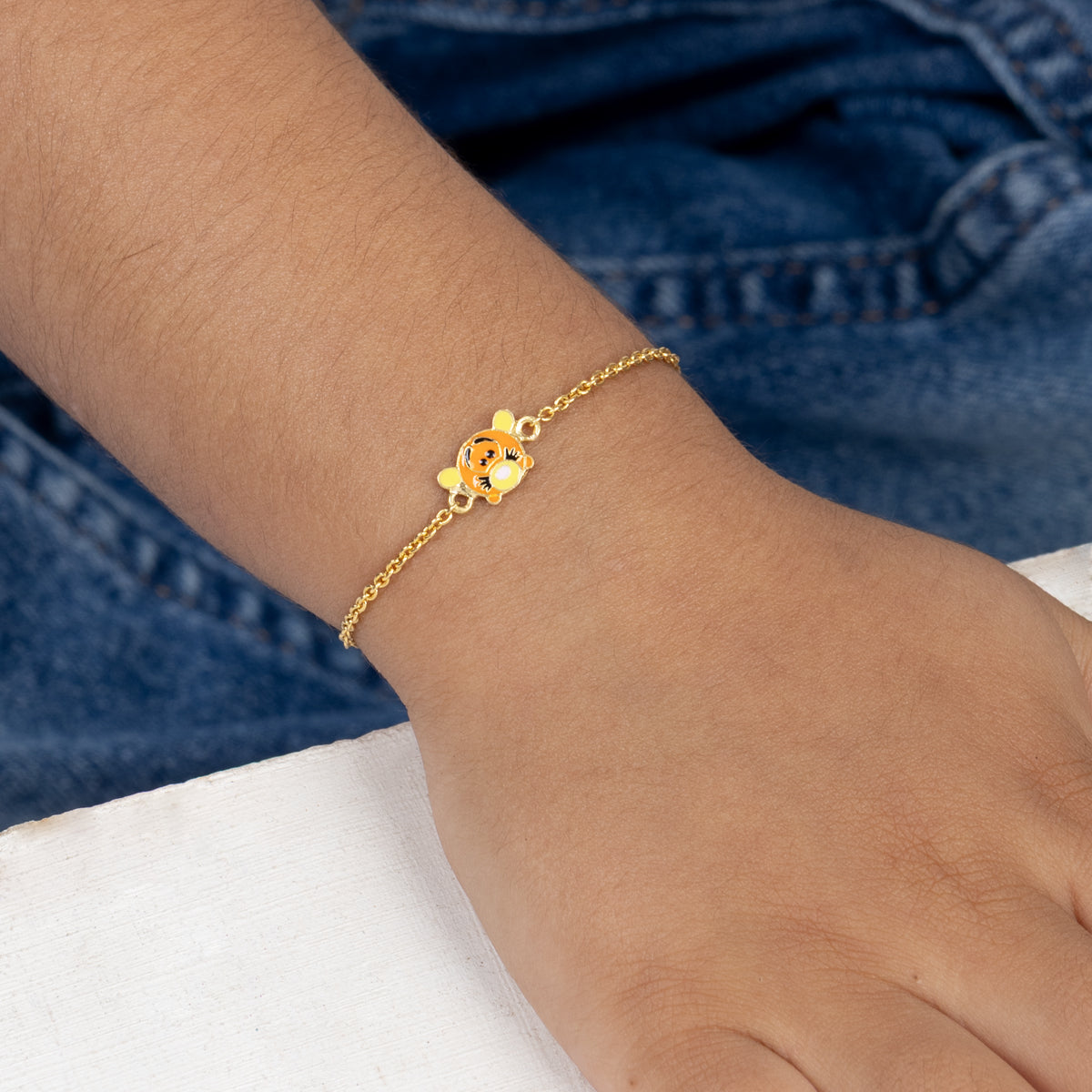 Tiny Jewels gold bracelet with a floral charm on a wrist against a blue denim background
