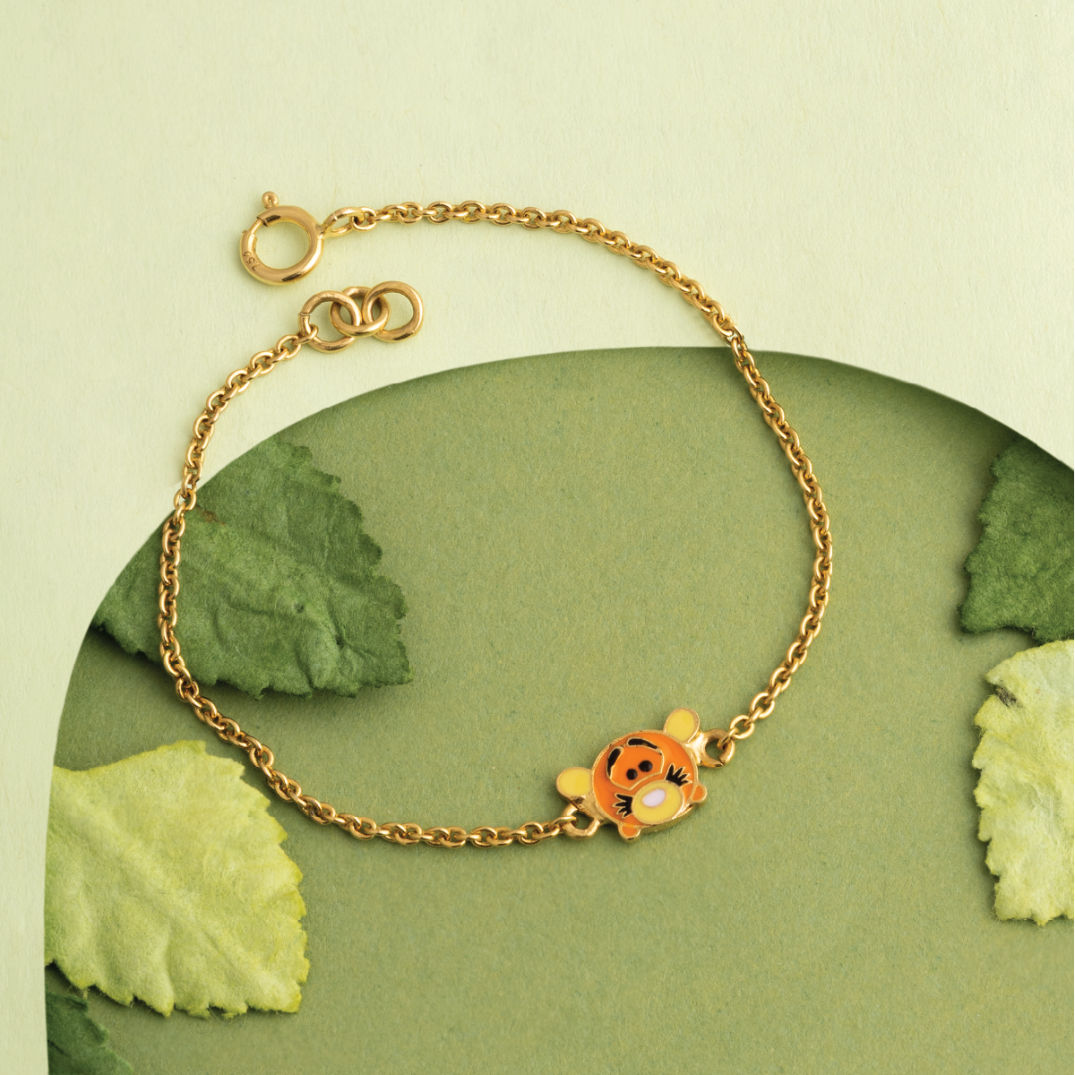 Tiny Jewels gold bracelet with a character charm on a green leaf background