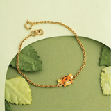 Tiny Jewels gold bracelet with a character charm on a green leaf background