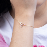 Tiny Jewels gold bracelet with a pink bow charm on a wrist against a white background