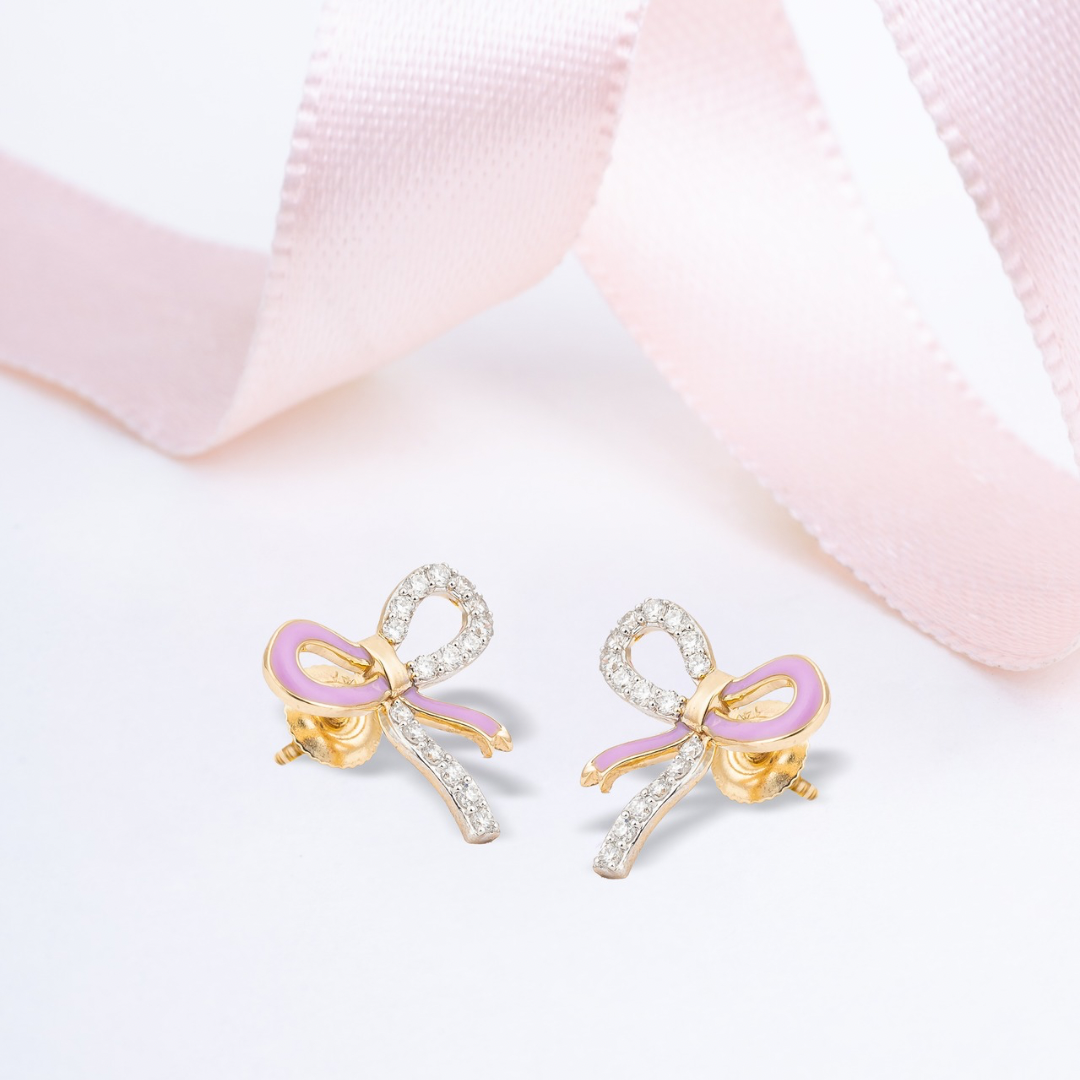 Tiny Jewels bow-shaped earrings with pink centers on a light pink fabric background
