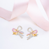 Tiny Jewels bow-shaped earrings with pink centers on a light pink fabric background