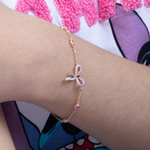 Tiny Jewels gold bracelet with a pink bow charm on a wrist against a colorful background