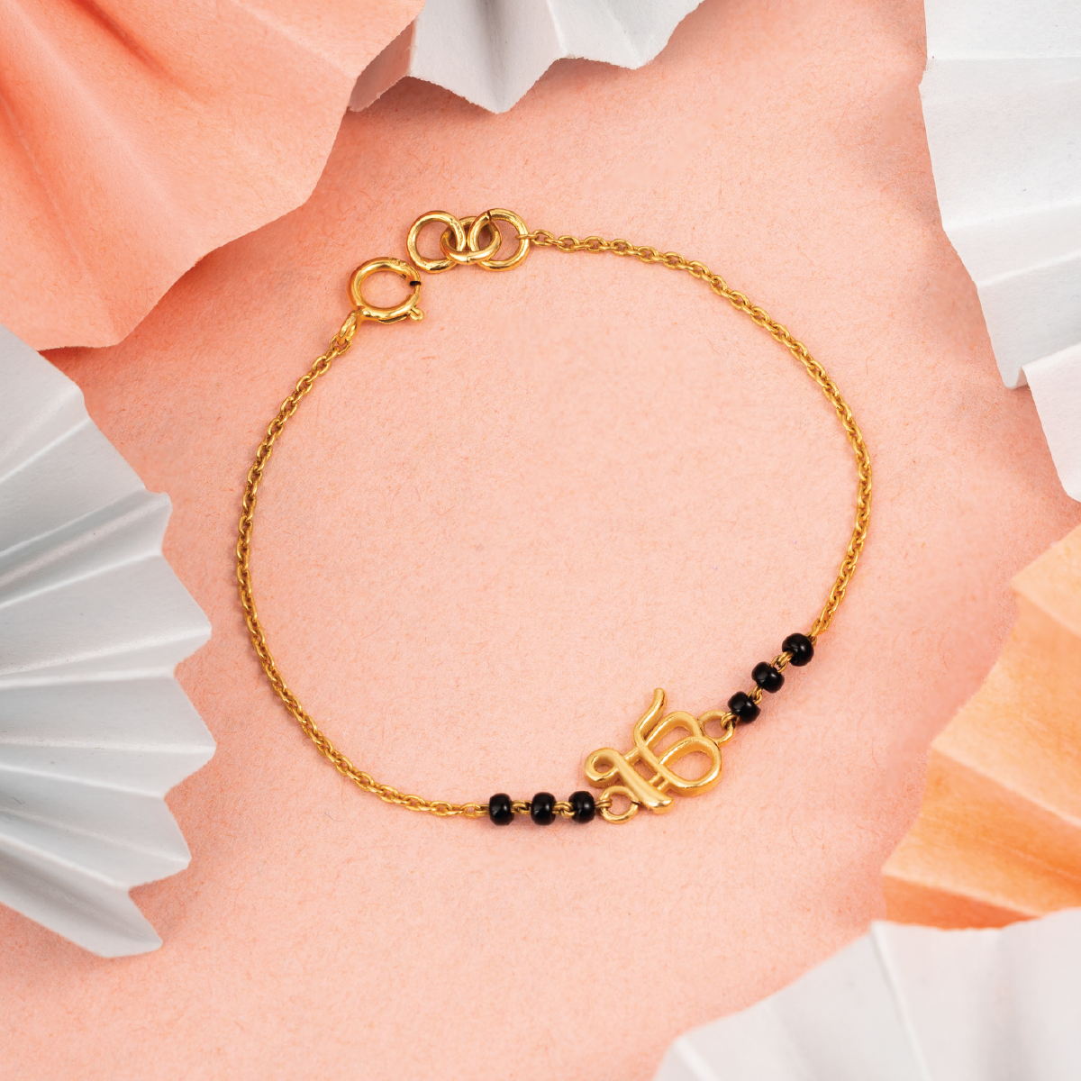 Tiny Jewels gold bracelet with black beads on a soft pink background