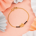Tiny Jewels gold bracelet with black beads on a soft pink background