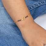 Tiny Jewels gold bracelet with black beads on a wrist against a denim background