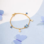 Tiny Jewels gold bracelet with blue charms on a light blue background