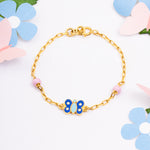 Tiny Jewels gold bracelet with a blue butterfly charm on a white background with flowers