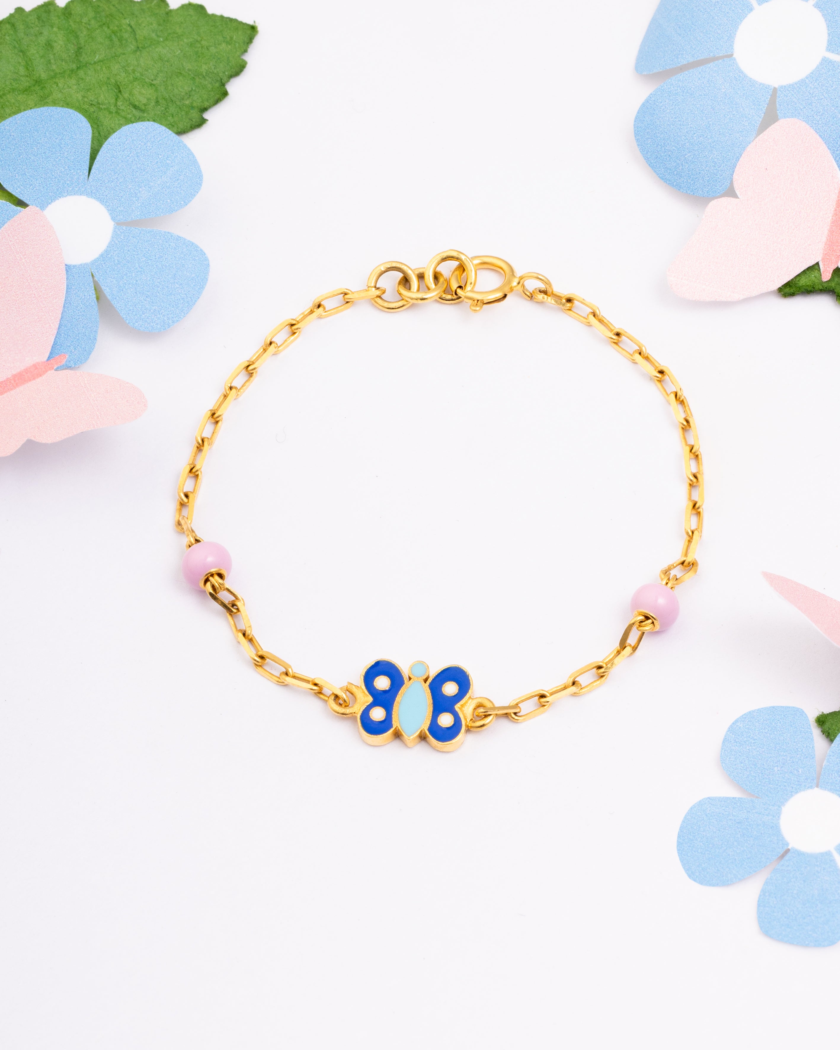 Tiny Jewels gold bracelet with a blue butterfly charm on a white background with flowers
