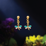 Tiny Jewels gold dragonfly-shaped earrings with turquoise wings on a dark background