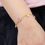 Tiny Jewels gold bracelet with colorful heart-shaped charms on a wrist against a black background