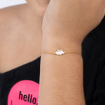 Tiny Jewels gold bracelet with colorful charms on a person's wrist, wearing a black top with a pink 'hello' graphic.