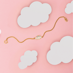 Tiny Jewels gold bracelet with a heart-shaped clasp on a pink background with white clouds