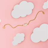 Tiny Jewels gold bracelet with a heart-shaped clasp on a pink background with white clouds