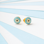 Tiny Jewels pair of turquoise and gold earrings on a light blue and white striped background