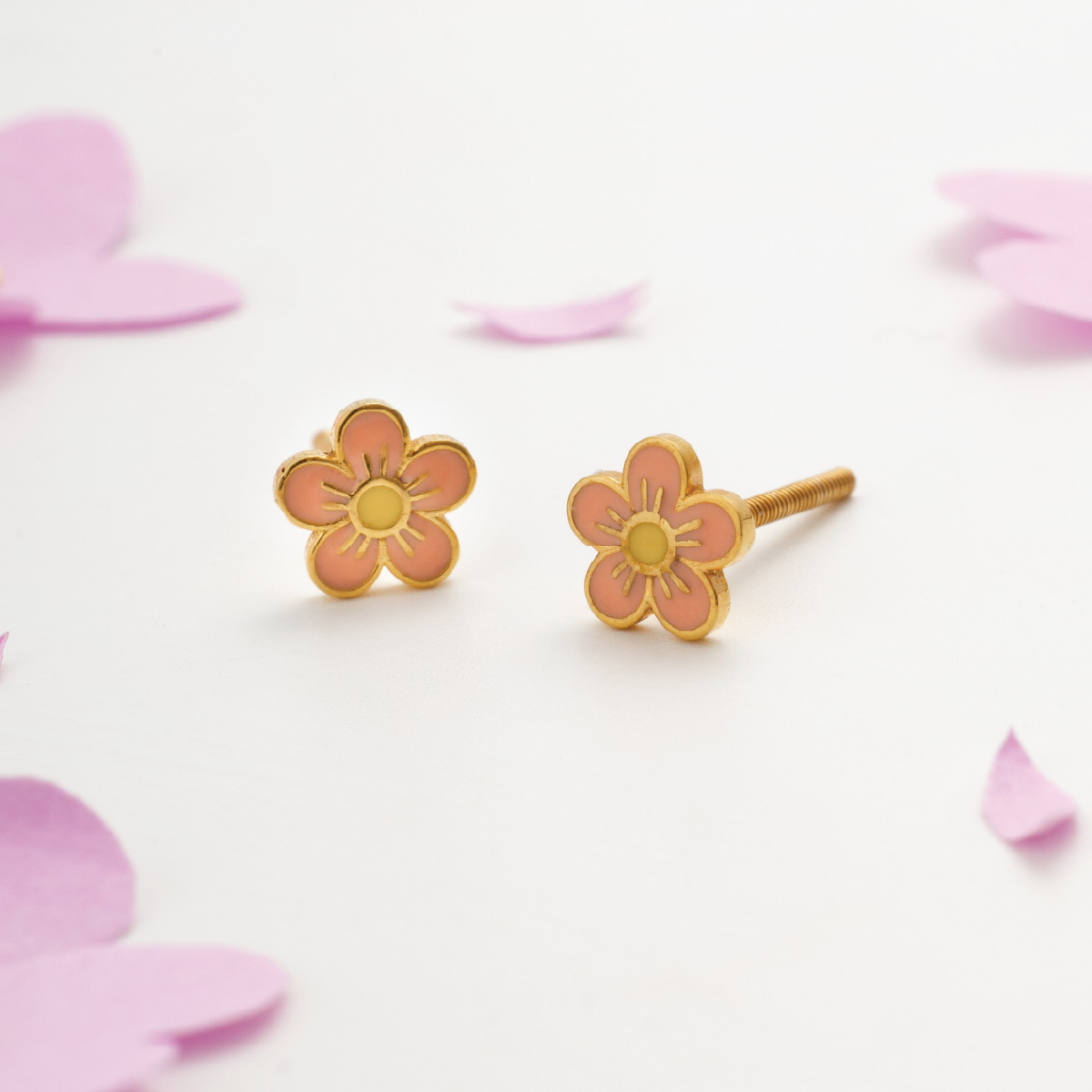 Tiny Jewels flower-shaped earrings on a light pink background with pink petals.