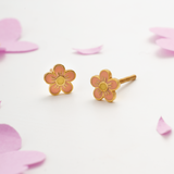 Tiny Jewels flower-shaped earrings on a light pink background with pink petals.