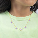 Tiny Jewels gold necklace with purple flowers worn by a person in a green shirt