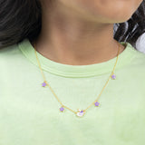 Tiny Jewels gold necklace with purple flowers worn by a person in a green shirt