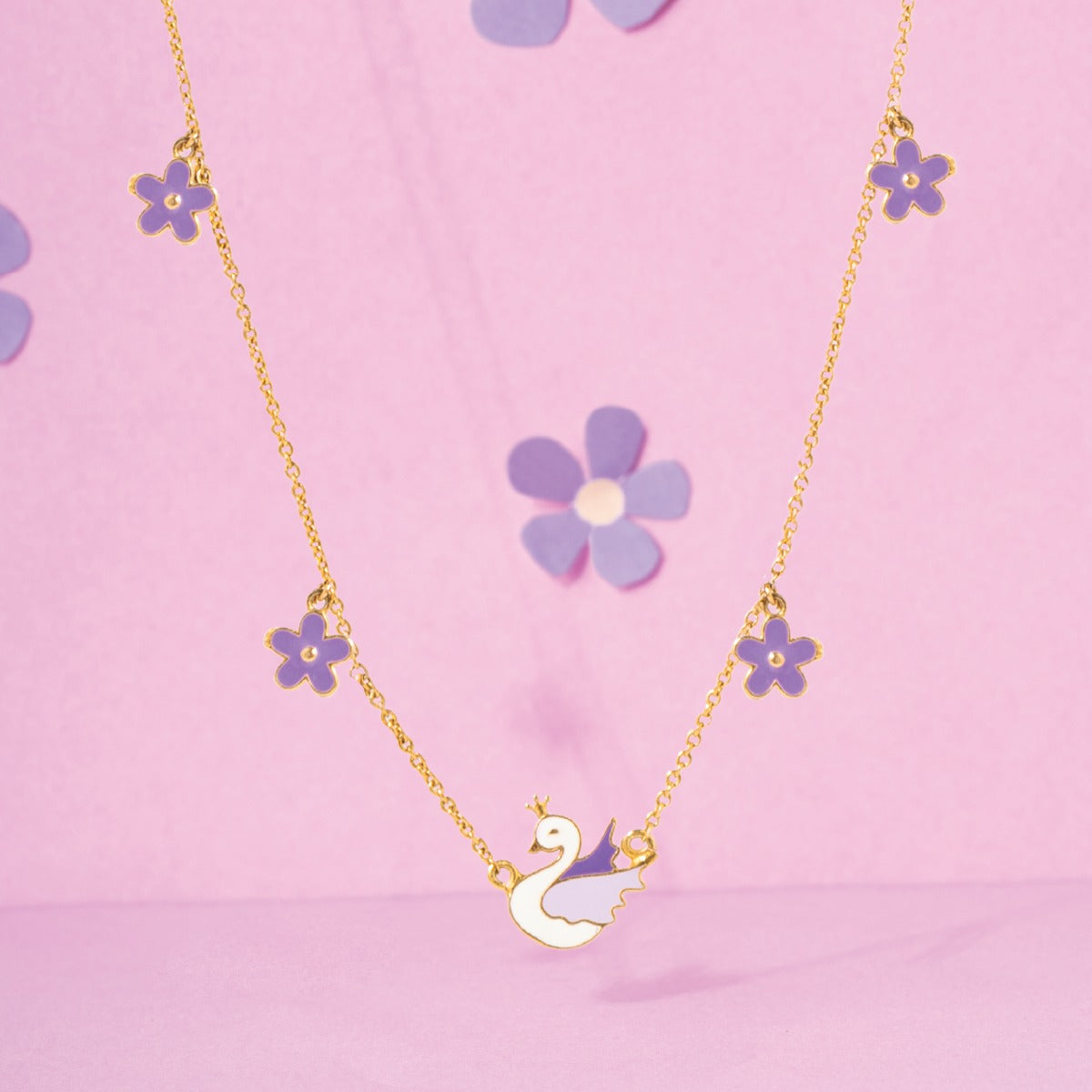 Tiny Jewels necklace with a swan pendant and flower-shaped pendants on a pink background